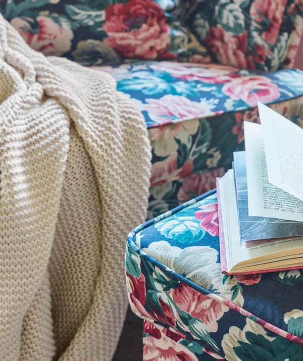 Light coloured IKEA INGABRITTA throw draped over the edge of a floral patterned sofa, near a footstool with an open book on it.