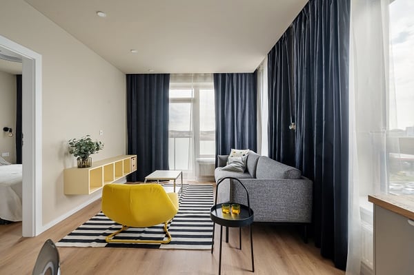 Light living room with yellow armachair, grey sofa, rug and blue curtains