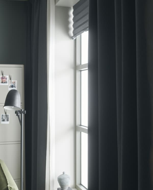 Light shines in through a window with light grey roller blinds, white sheer curtains and dark grey room darkening curtains.