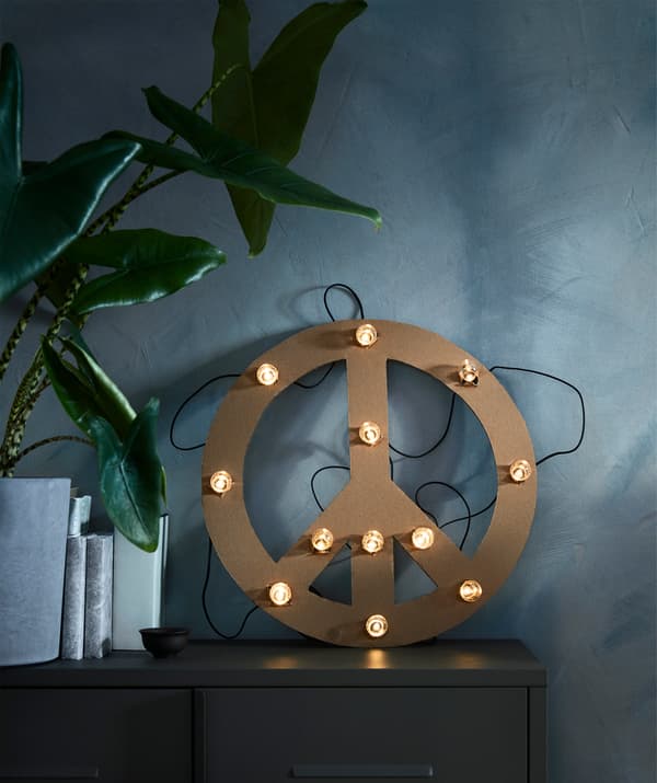 L'illuminazione a LED BLÖTSNÖ con 12 luci a batterie su una sagoma di carta posata su un mobile. Accanto ci sono dei libri accostati e una pianta.