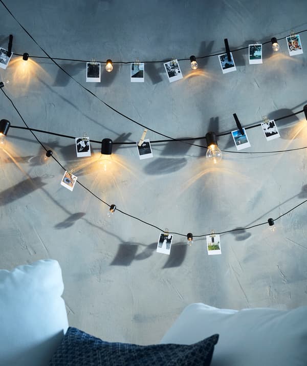 L'illuminazione a LED SVARTRÅ con 12 luci in nero su dei fili a cui sono appese delle foto. Sotto, tre cuscini.