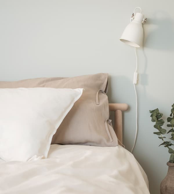 Linen pillowcases in white and beige shown together with a white quilt cover in a birch bed, against a light green wall.