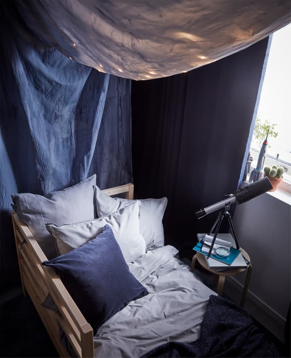 Linge de lit et taies d’oreiller ÄNGSLILJA. Un lit et un ciel de lit en tissu teint en bleu foncé avec des rideaux occultants.