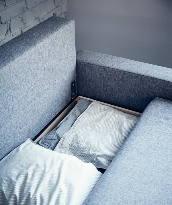 Linge de lit rangé dans un canapé convertible gris.