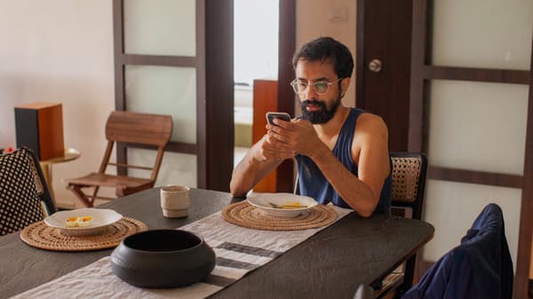 'Link to '16 surprising facts about life at home in 2021' - image of a a man with dark hair and a beard browsing his mobile phone at the kitchen table.
