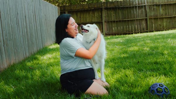 Link to '5 ways to make your home the key to a balanced life' - image of a smiling woman playing with a white dog on green grass.