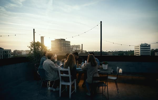 Link to 'a better world starts at home' IDEA - image of a group of friends gathered around a rooftop table at sunset.