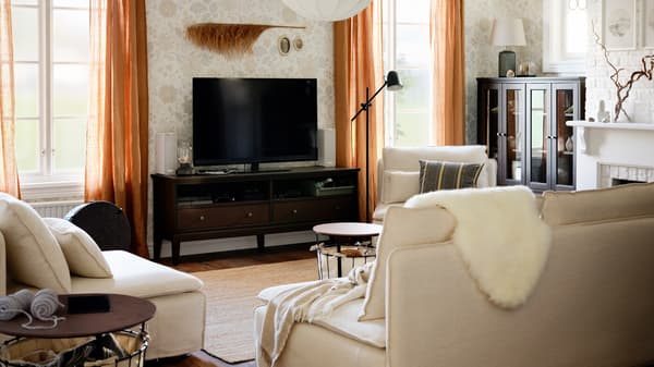 Link to 'A living room with clutter-free calm for everyone' - image of  a TV bench between two windows in a living room with beige sofas.