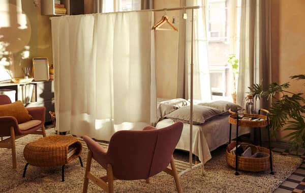 Link to 'How to host overnight guests in a small-space home' IDEAS blog - image of a living room where a wide bed stands behind a room divider.