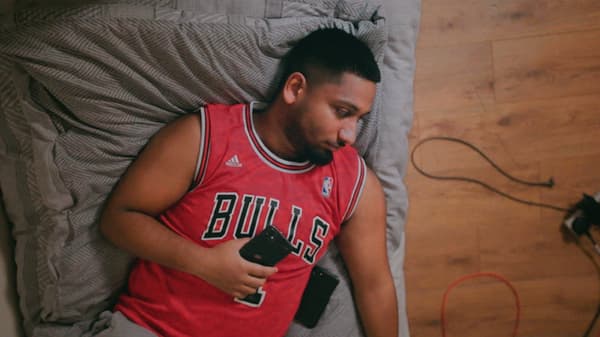 Link to 'Our search for the secret to a balanced life at home' - image of a young man with a beard and a red sports shirt relaxing on a grey sofa.