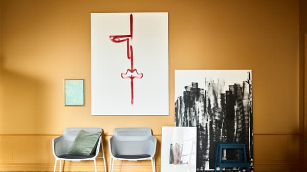 Link to 'Personalize it' - image of canvases hanging and leaning on an ochre wall with black and red brushstrokes on them and two chairs in front of them.