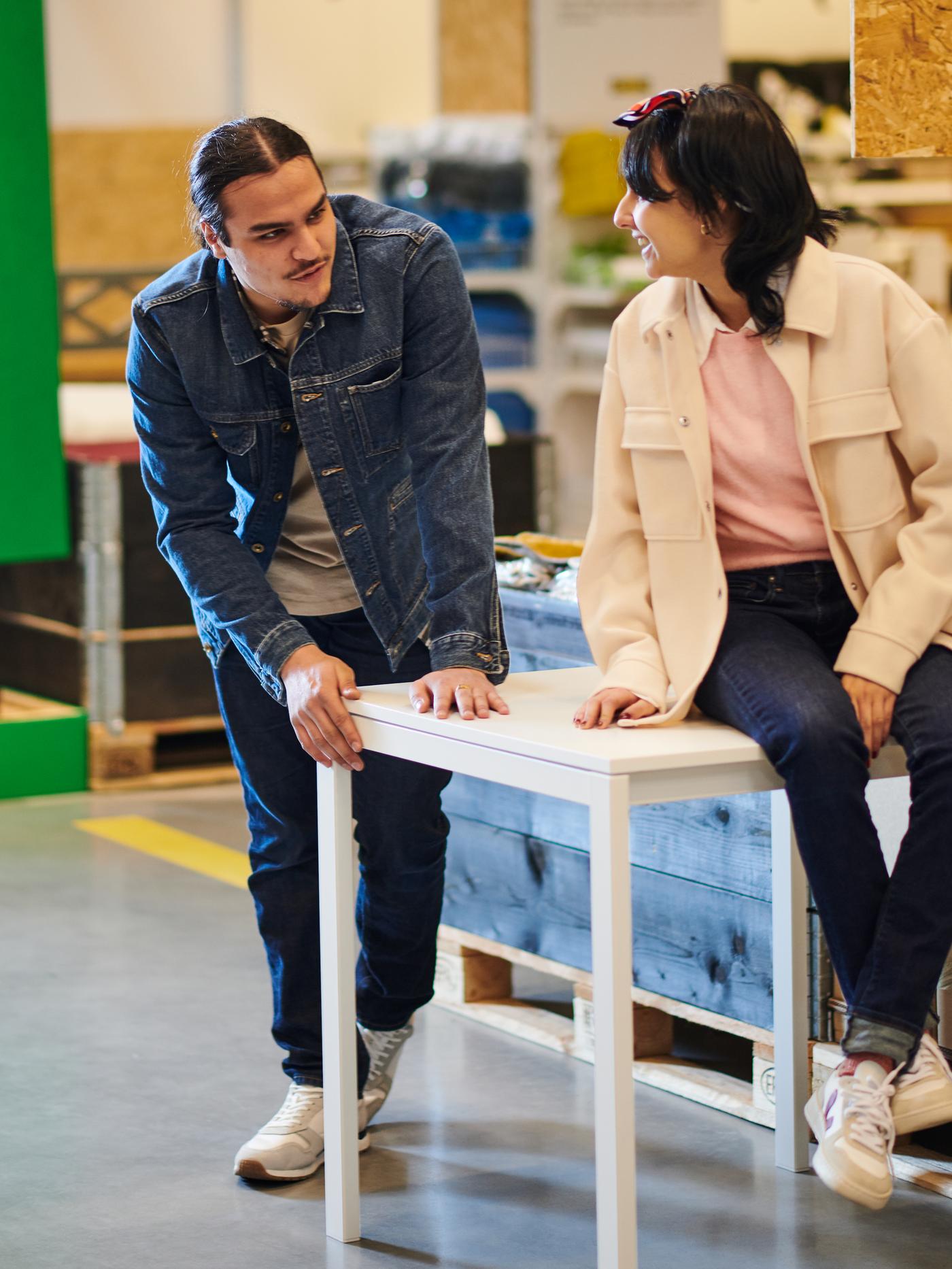 L’intérieur d’un magasin avec une femme assise sur une table et un homme debout à côté.