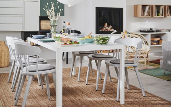 L’intérieur d’un salon et salle à manger deux en un avec cheminée, rangements muraux et une table de salle à manger TINGBY entourée de chaises OMTÄNKSAM.