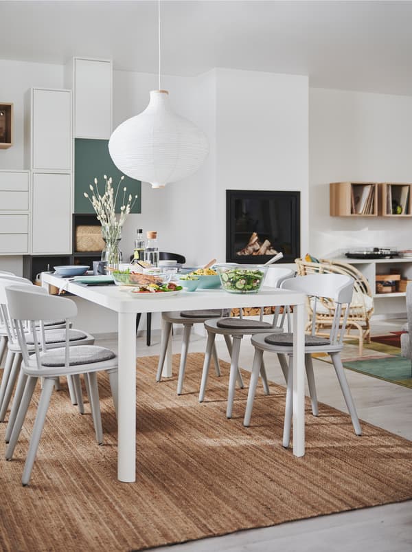L’intérieur d’un salon et salle à manger deux en un avec cheminée, rangements muraux et une table de salle à manger TINGBY entourée de chaises OMTÄNKSAM.