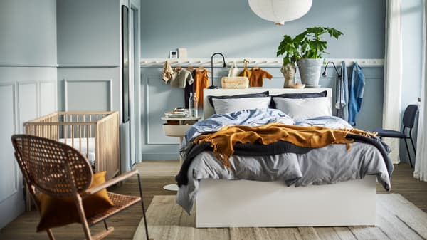 Lit blanc, lampe blanche, patère à boutons, chaise berçante en rotin et lit à barreaux SNIGLAR dans une chambre bleu clair.