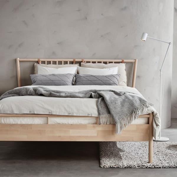 Lit deux places en bois avec une parure de lit blanche et un plaid gris.