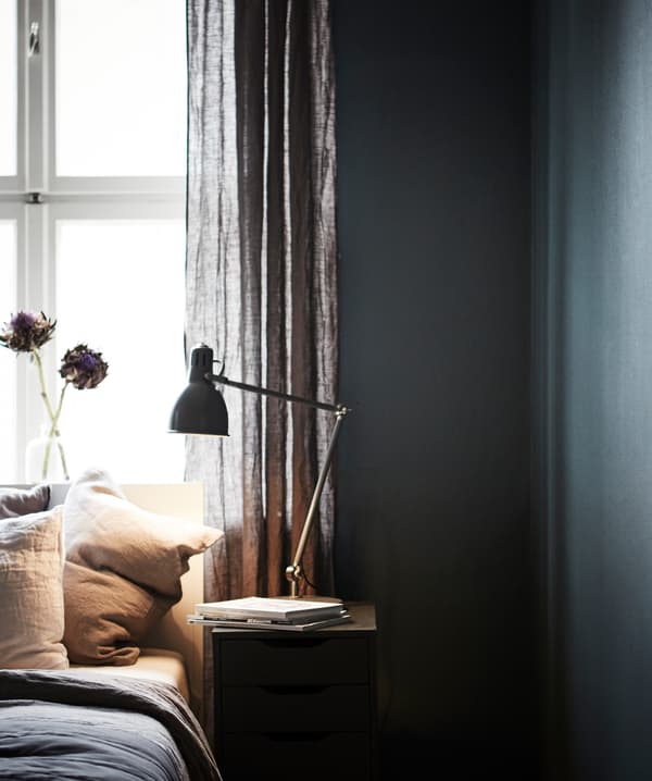 Lit et table de chevet devant une fenêtre, avec mur foncé tout autour.