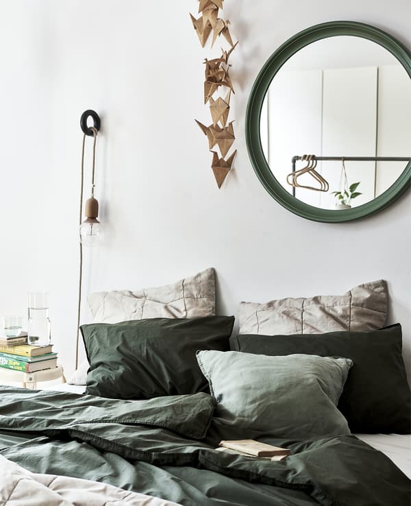 Lit garni de linge de lit vert et miroir vert au mur.