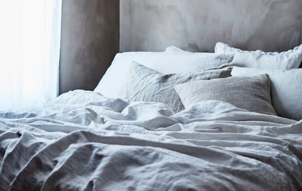 Lit garni d'un linge de lit gris et blanc.