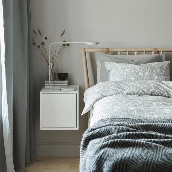 Lit habillé de linge de lit gris en plusieurs couches et table de chevet blanche.