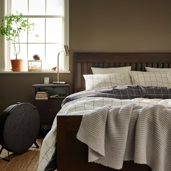 Lit IDANÄS brun foncé recouvert de linge de lit VITKLÖVER sur un tapis tissé à plat LOHALS, à côté d’un purificateur d’air STARKVIND noir.