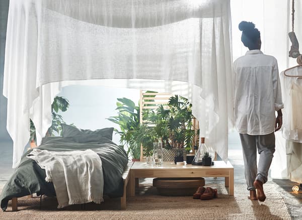 Lit placé sous un ciel de lit drapé blanc et plantes vertes.