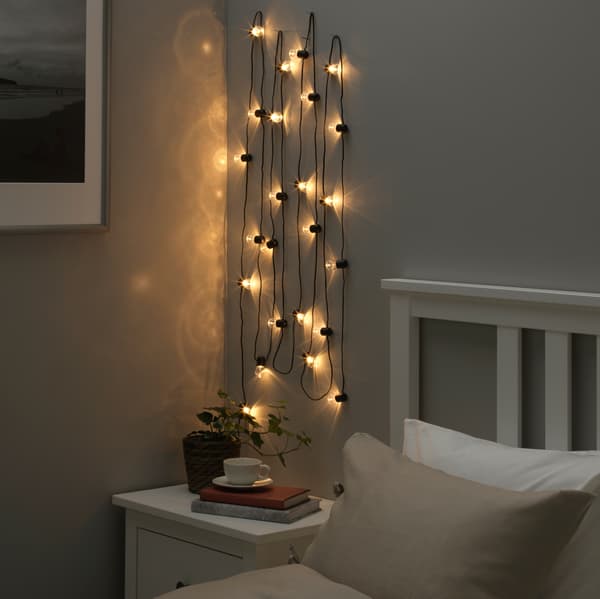 Lit string lights hung on a wall above a nightstand beside a bed.