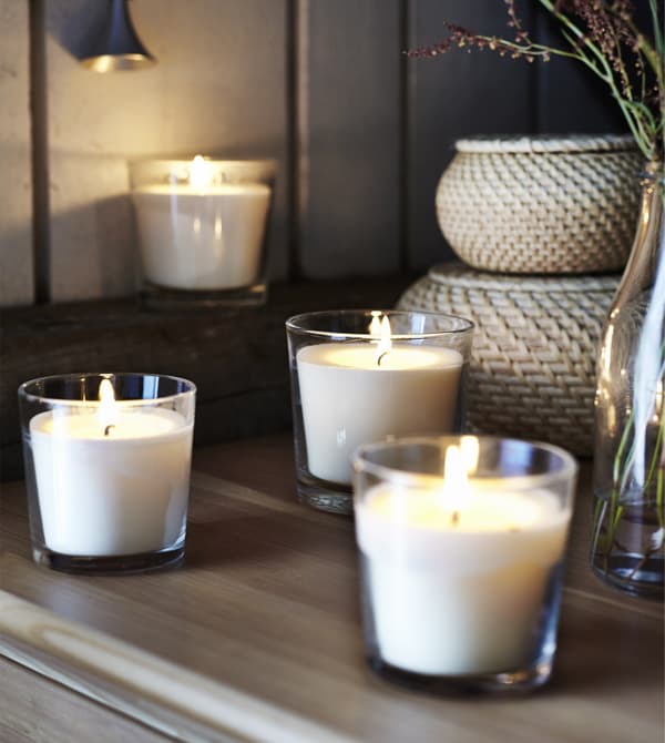 Lit vanilla-scented candles in glass cups sit in a rustic-style bedroom.