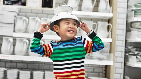 little boy wearing a striped shirt placing a white colander on his head