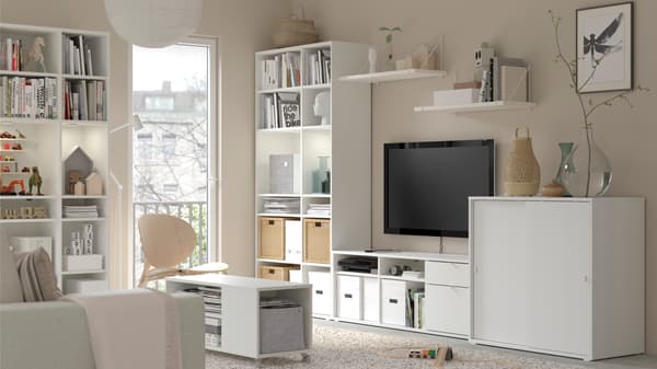 Living con una combinación de muebles blanca con un televisor. Dentro de los estantes hay cajas de organización, libros y artículos decorativos.