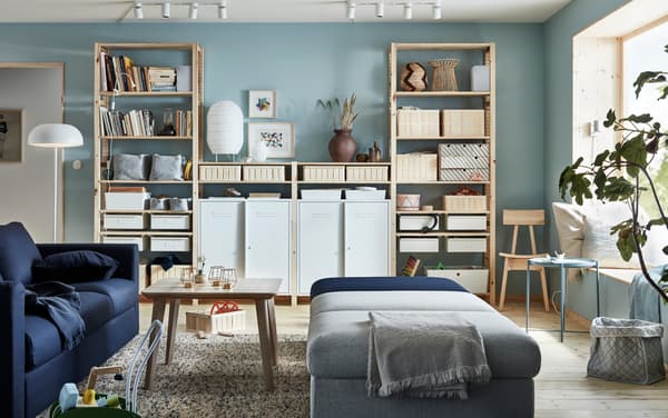 Living donde hay un sofá azúl oscuro VIMLE, una mesa de centro de madera y módulos de sofá grises y azul para sentarse. Un mueble grande atrás de madera lleno de libros y cajoneras organizadoras.
