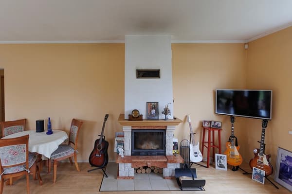 Living room before the makeover: a round dining table stands next to the fireplace, along with four guitars and framed pictures; a TV is mounted in the corner.