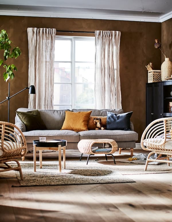 Living room in an earthy-shades color scheme with decorations, storage, seating, side table, a footstool and a plant.