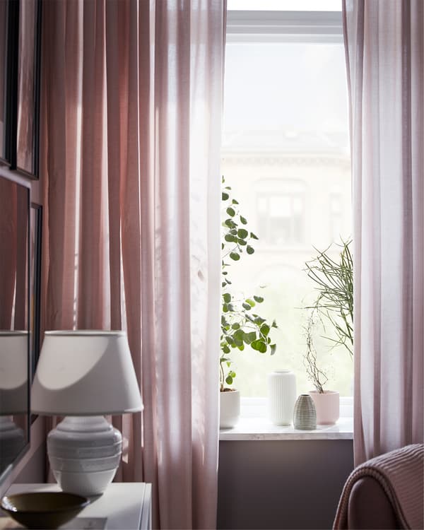Living room windows, with HANNALILL curtains in pink filtering the light, and some plants and plant pots in the windowsill.
