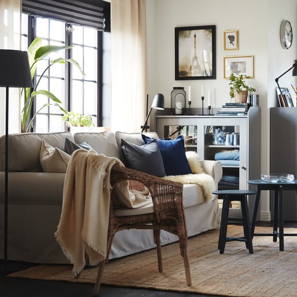 Living room with a light beige sofa-bed, a jute rug, a rattan/bamboo chair and two cabinets and a chest of drawers in grey.