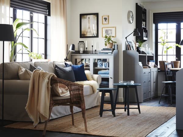Living room with a light beige sofa-bed, a jute rug, a rattan/bamboo chair and two cabinets and a chest of drawers in grey.
