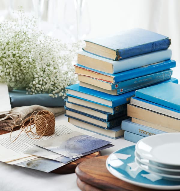 Livres bleus, gypsophile et assiettes, posés sur la table qui va être dressée.