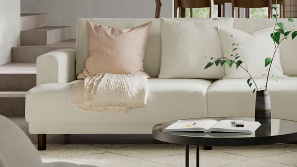 Ljusbeige UPPÅKRA soffa med ljusa kuddar och ett svart runt soffbord i ljust vardagsrum. 