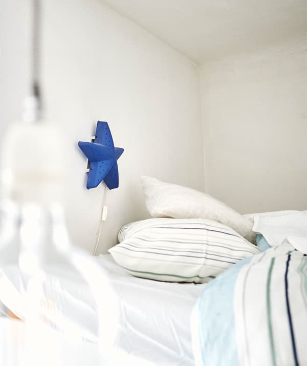 Llum blau en forma d'estrella en una paret a sobre d'un llit amb teixits estampats.