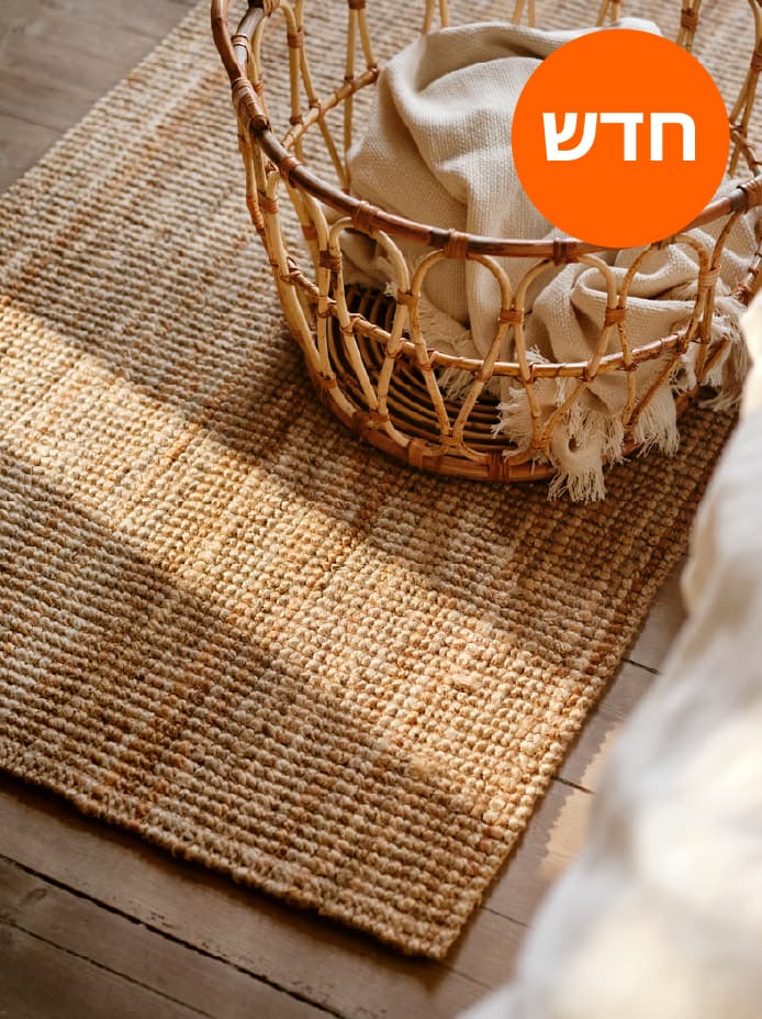 שטיח LOHALS טבעי קצר-סיבים, מעליו סלסילת SNIDAD בעבודת יד מראטן ובתוכה שמיכת טלוויזיה.