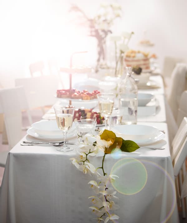 Long table set for dessert in romantic, lavish way in all white chairs, tables and textiles, with various floral decorations.