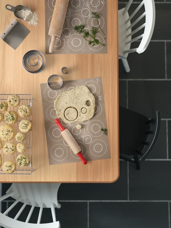 Looking down on a traditional kitchen table that is being used to do some baking with rolling pins and dough