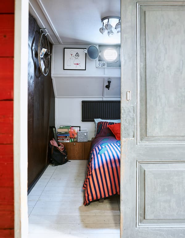 Looking through a doorway to a bedroom with red bedding and a dark wall.