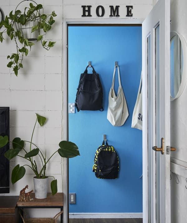 Looking through a white doorway to a blue wall where bags hang on hooks at different heights.