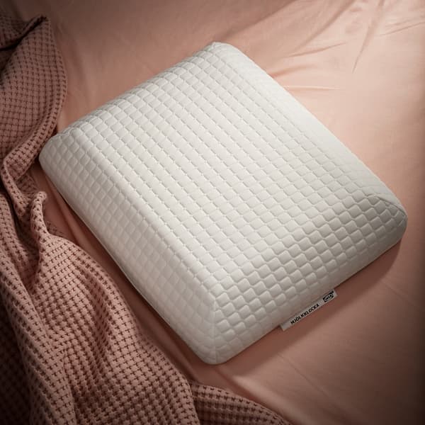 L'oreiller ergonomique de forme unique IKEA MJÖLKKLOCKA posé sur du linge de lit rose poudré.