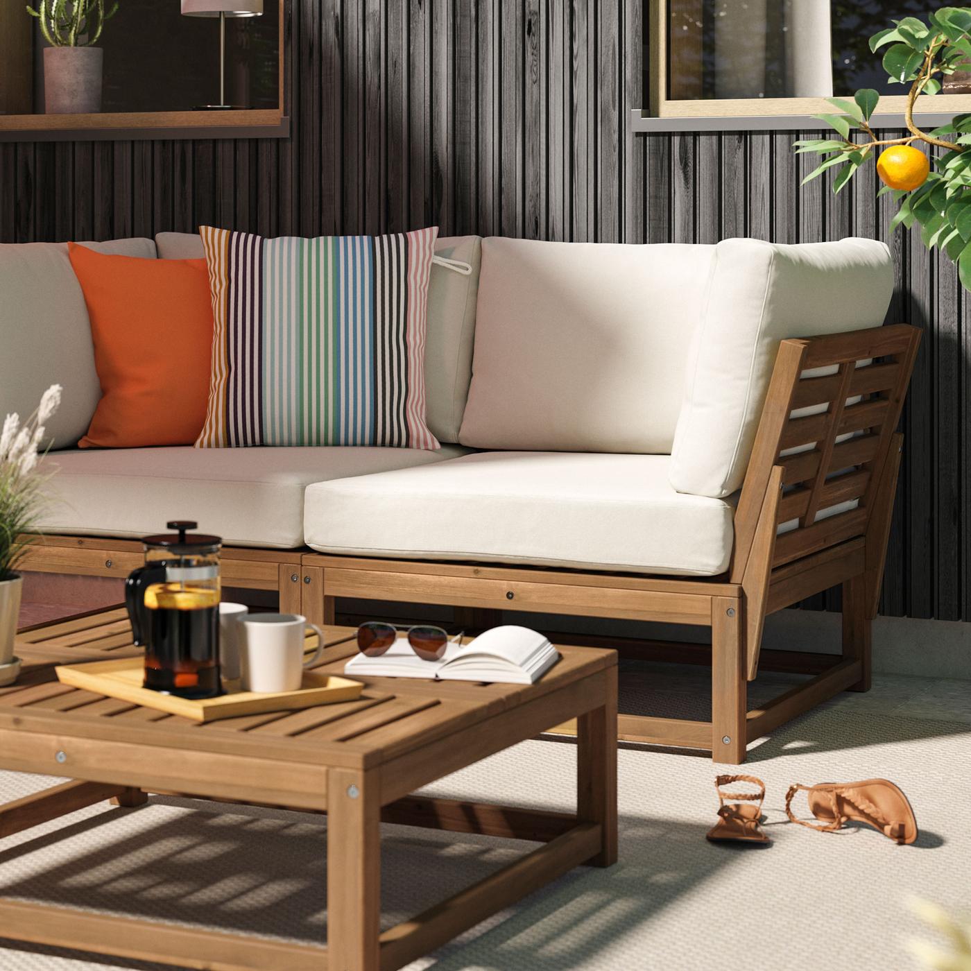 Loungesoffa och soffbord i trä med ljusbeiga dynor mot svart trävägg. 