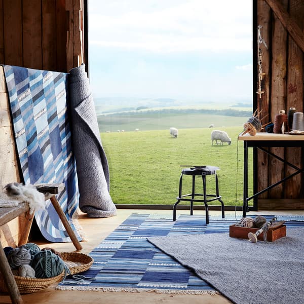 LOVRUP wool and 20% cotton rugs and TRANGET wool rugs in shades of blue are shown on a floor and against a wall in a barn.