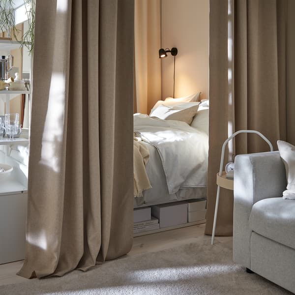 Łóżko, nieco schowane za beżową zasłoną, która je otacza, aby stworzyć przytulny kącik do spania.