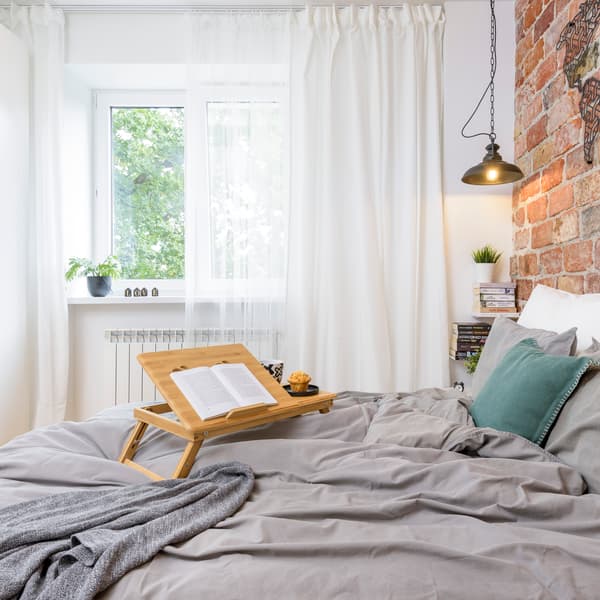 Łóżko z duża ilością tekstyiów na którym stoi taca z podstawką pod ksiązkę.