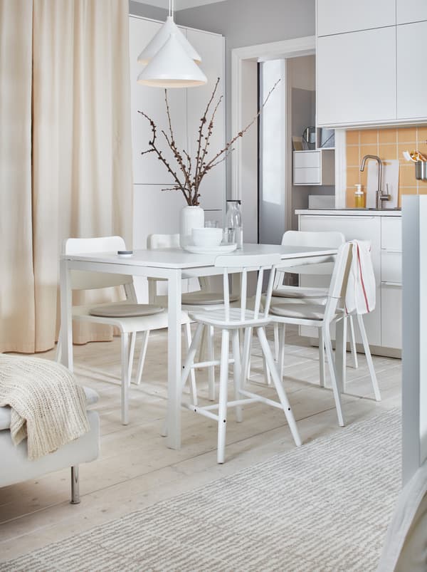 Lumineux et blanc, un appartement décoré d’une table MELLTORP et de chaises TEODORES entre une kitchenette et un lit.